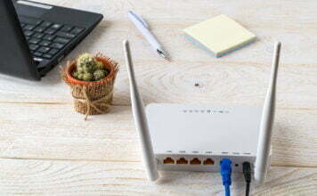 White Wi-Fi wireless router near laptop on a white wooden table. Wlan router with internet cables plugged in on a table in a home or office