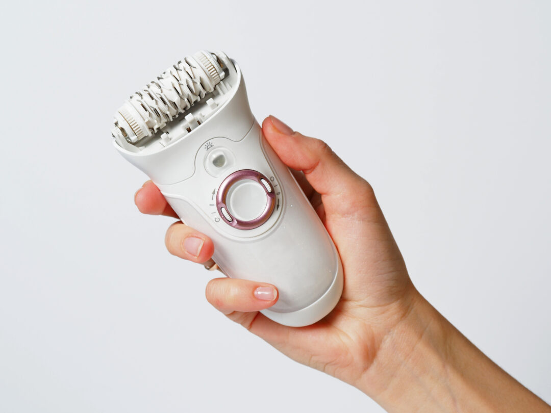 Female epilator white in a female hand on a white background. Electric hair removal device. Concept of skin care and female beauty. Women's suffering.