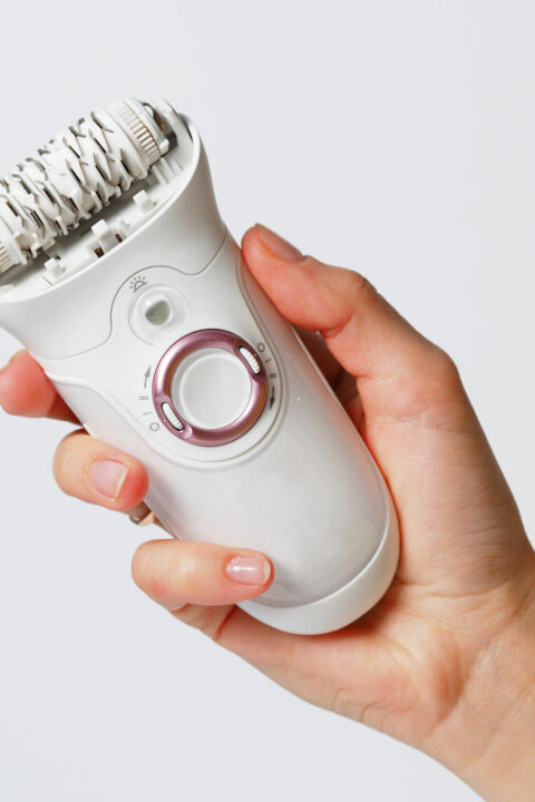 Female epilator white in a female hand on a white background. Electric hair removal device. Concept of skin care and female beauty. Women's suffering.